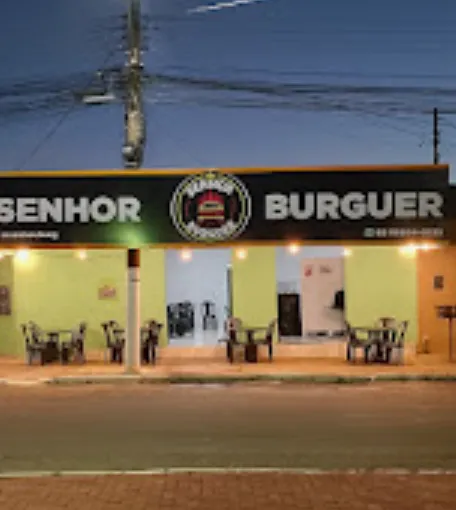 Fachada do Senhor Burguer à noite, com letreiro iluminado e mesas na calçada